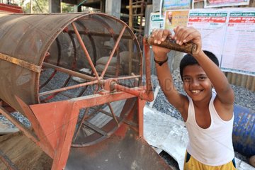 Smiling boy turning the crank of a sieve India