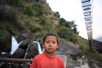 Portrait of a boy under a suspension bridge Syanje Nepal