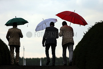 Hoppegarten  Maenner schuetzen sich mit Regenschirmen vor dem Regen