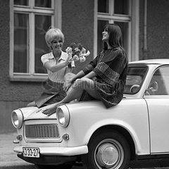 Berlin  DDR  Modeaufnahme  Modefotografie  junge Frau reicht ihrer auf einem Trabant sitzenden Freundin Blumen