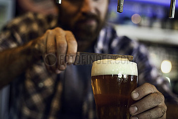 Man with a knife removing froth from a beer glass