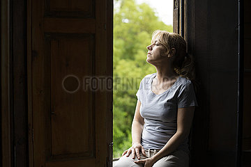 Thoughtful woman sitting on window