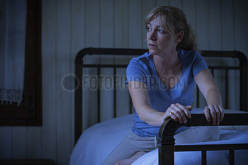 Thoughtful sad woman sitting on bed