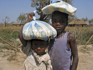 Angolan children carry bags of food on their heads. Feeding centres and other humanitarian aid were organised in Angola after widescale malnutrition during and following the countrys civil war.
