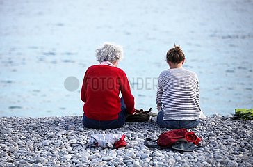 Alte und junge Frau sitzen am Strand