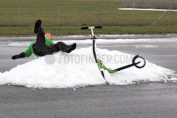 Berlin  Deutschland  Junge faellt im Winter von seinem Roller auf einen Schneehaufen