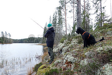 Braenna  Schweden  Junge angelt in Begleitung seines Hundes an einem See