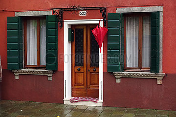 Burano  Italien  Regenschirm haengt vor der Tuer eines roten Hauses