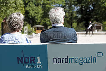 Redefin  Deutschland  Mann und Frau sitzen auf einer Bank mit Werbung des NDR und verfolgen ein Dressurturnier