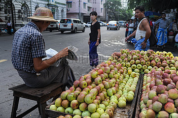 Yangon  Myanmar  Ein Mann liest Zeitung neben seinem Obststand