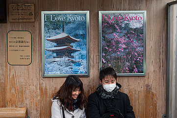 Kyoto  Japan  Paar sitzt an einer Bushaltestelle vor Werbeplakaten mit dem Slogan I Love Kyoto