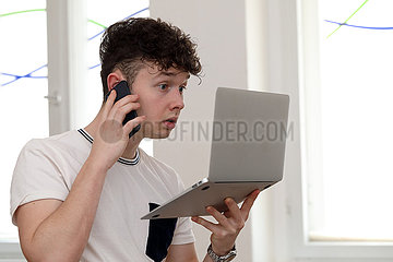 Berlin  Deutschland  Teenager telefoniert mit seinem Smartphone und schaut dabei fassungslos auf sein Tablet
