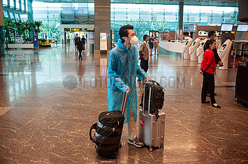 Singapur  Republik Singapur  Passagier mit Mundschutz und Regenmantel vor dem Check-in am Flughafen Changi
