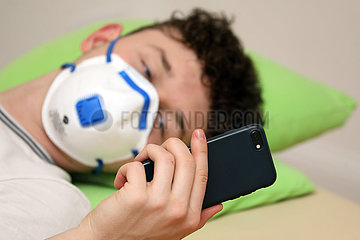 Berlin  Deutschland  junger Mann mit Atemschutzmaske schaut auf sein Mobiltelefon