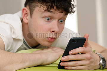 Berlin  Deutschland  Teenager schaut im Bett ueberrascht auf sein Smartphone