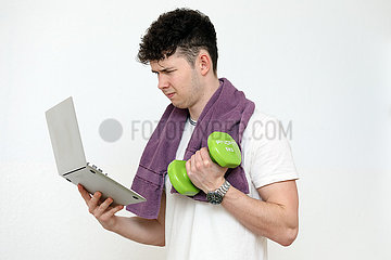 Berlin  Deutschland  Teenager trainiert mit einer Hantel und schaut dabei auf sein Tablet