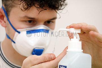 Berlin  Deutschland  junger Mann mit Atemschutzmaske desinfiziert sich die Haende