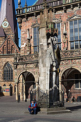 Deutschland  Bremen - Weitgehend von Corona geleerte Altstadt  Mann mit Mundschutz sitzt vor dem Roland  dahinter das Rathaus
