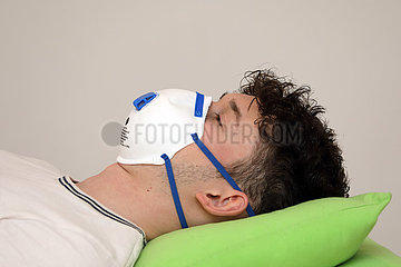 Berlin  Deutschland  Junger Mann mit Atemschutzmaske liegt im Bett