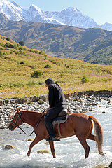 Adishi  Georgien  Mann ueberquert auf einem Pferd einen Gletscherfluss am Tetnuldi