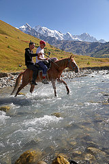 Adishi  Georgien  Maenner ueberqueren auf einem Pferd einen Gletscherfluss am Tetnuldi