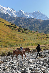Adishi  Georgien  Mann fuehrt sein Pferd bei einem Ausritt am Tetnuldi