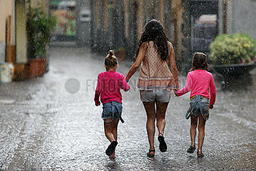 Orvieto  Italien  Frau laeuft mit zwei Maedchen an der Hand bei Regenwetter auf einer Strasse