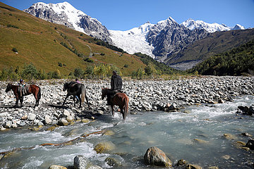 Adishi  Georgien  Maenner ueberqueren auf ihren Pferden einen Gletscherfluss am Tetnuldi