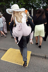 Ascot  Grossbritannien  Mann traegt eine modisch gekleidete Frau in High Heels Huckepack