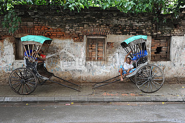 Kolkata (Kalkutta)  Indien  Zwei Rikschalaeufer pausieren in ihren traditionellen Rikschas am Strassenrand