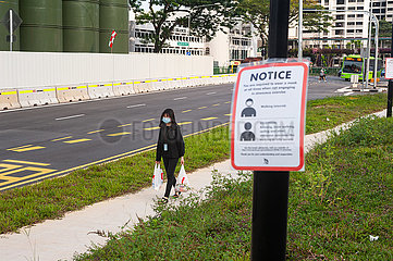 Singapur  Republik Singapur  Frau mit Mundschutz hinter Hinweisschild zur Maskenpflicht im Freien