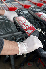 Berlin  Deutschland - Haende mit Einmal-Handschuhen am Griff eines Einkaufswagens vor einem Supermarkt