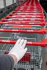 Berlin  Deutschland - Hand mit einem Einmal-Handschuh am Griff eines Einkaufswagens vor einem Supermarkt