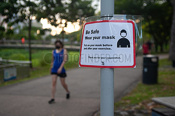 Singapur  Republik Singapur  Frau mit Mundschutz neben Hinweisschild zur Maskenpflicht im Freien
