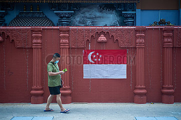 Singapur  Republik Singapur  Mann mit Mundschutz geht an einer Nationalflagge vorbei