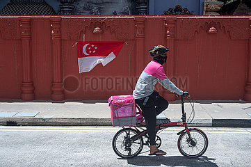 Singapur  Republik Singapur  Radfahrer mit Mundschutz faehrt an einer Nationalflagge vorbei