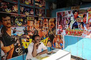 Mumbai  Indien  Mann isst Eis vor einem kleinen Kino mit Filmplakaten im Dharavi-Slum