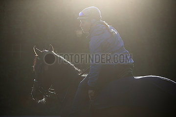 Hoppegarten  Pferd und Reiterin bei der Morgenarbeit im Gegenlicht