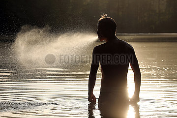 Walkmuehle  Deutschland  Jugendlicher spuckt bei Sonnenuntergang im Baalsee Wasser in die Luft