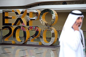 Dubai  Vereinigte Arabische Emirate  Mann in Landestracht laeuft an einem Werbeaufsteller fuer die Expo 2020 vorbei