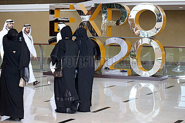 Dubai  Vereinigte Arabische Emirate  Einheimische laufen an einem Werbeaufsteller fuer die Expo 2020 vorbei