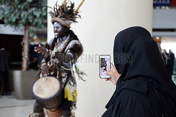 Dubai  Vereinigte Arabische Emirate  Einheimische Frau fotografiert einen afrikanischen Trommler mit ihrem Smartphone