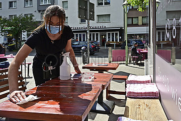 Deutschland  Nordhrein-Westfalen  Essen - Kellnerin desinfizert Tische mit Mund- und Nasenschutz in einem Cafe waehrend der Coronapandemie