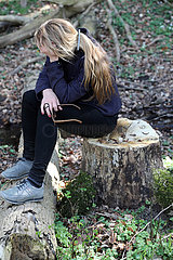 Neu Kaetwin  Deutschland  Frau sitzt verzweifelt im Wald allein auf einem Baumstumpf