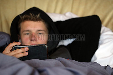 Dranse  Deutschland  Teenager liegt angezogen im Bett und schaut sein Smartphone