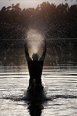 Dranse  Deutschland  Silhouette: Jugendlicher springt am Abend aus einem See heraus und spuckt Wasser in die Luft