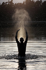 Dranse  Deutschland  Silhouette: Jugendlicher springt am Abend aus einem See heraus und spuckt Wasser in die Luft