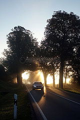 Neu Heinde  Deutschland  PKW faehrt bei Sonnenaufgang auf einer Landstrasse