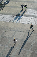 Berlin  Deutschland - Personen mit langen Schatten laufen ueber einen Platz.