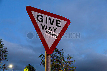 Grossbritannien  Nordirland  Belfast - Verkehrsschild Give Way (Vorfahrt Beachten) mit Aufkleber  der den Gebrauch der gaelischen Sprache propagiert